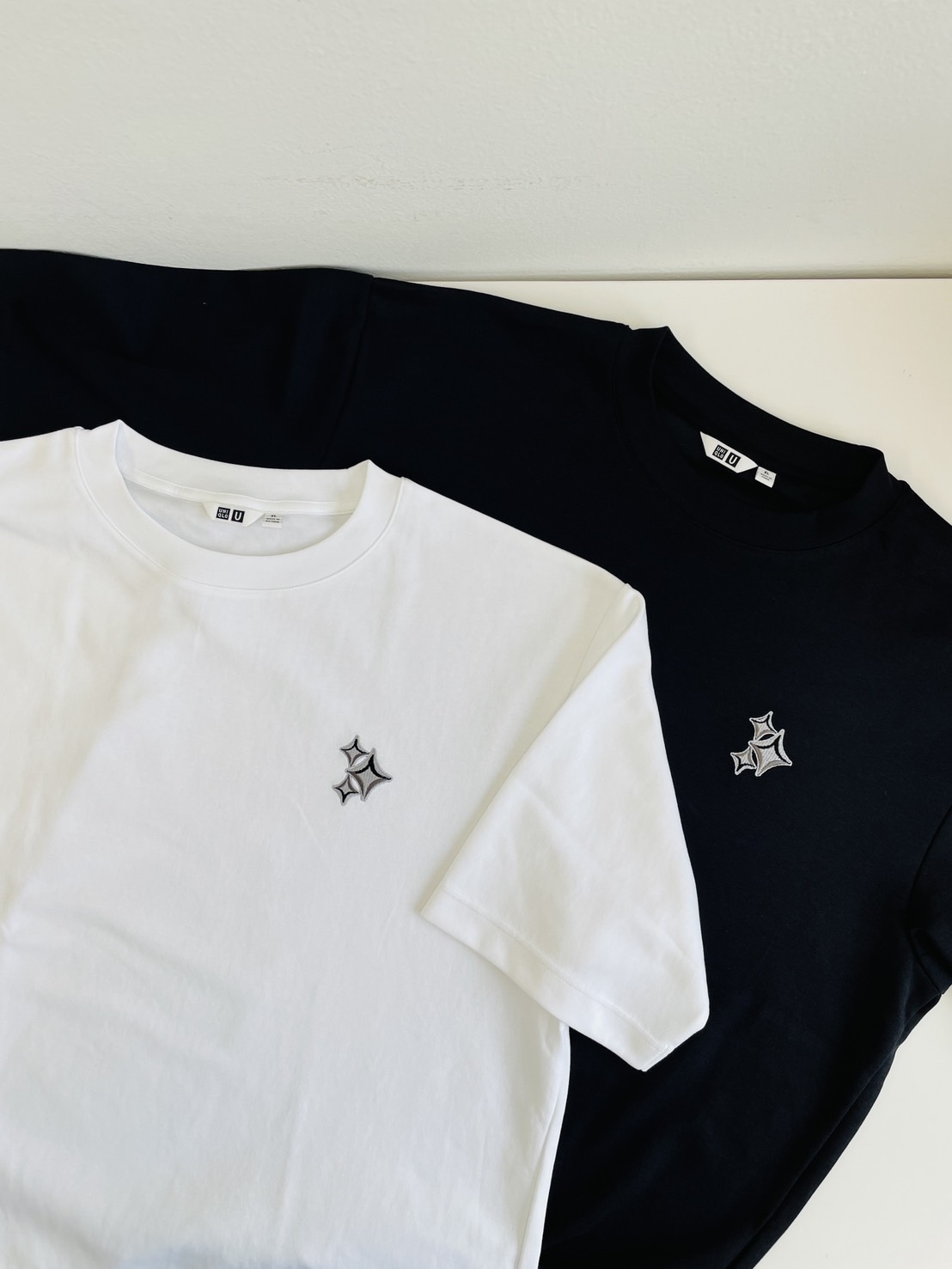 White and black T-shirts with the same embroidered three-star motif